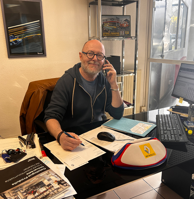 Homme souriant avec des lunettes au téléphone, assis à un bureau avec des papiers à Saint-Orens près de Toulouse en Haute-Garonne 31