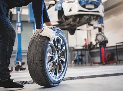 Mécanicien en gants blancs manipulant un pneu, voiture soulevée en arrière-plan à Saint-Orens près de Toulouse en Haute-Garonne 31