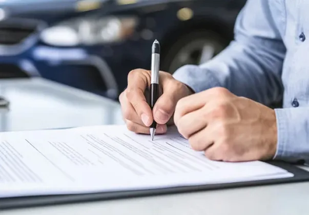 Gros plan d'une personne signant des papiers sur un bureau avec une voiture en arrière-plan à Saint-Orens près de Toulouse en Haute-Garonne 31