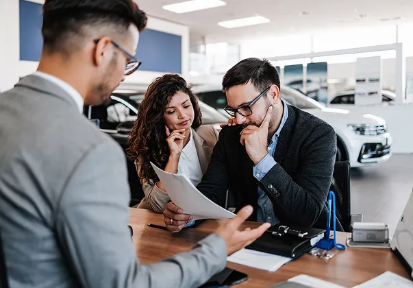 Couple examinant des documents avec un vendeur dans un concessionnaire automobile à Saint-Orens près de Toulouse en Haute-Garonne 31