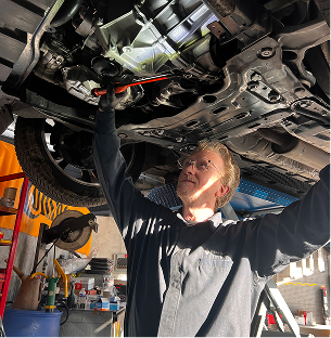 Mécanicien avec des lunettes travaillant sous une voiture sur un pont élévateur dans un garage à Saint-Orens près de Toulouse en Haute-Garonne 31