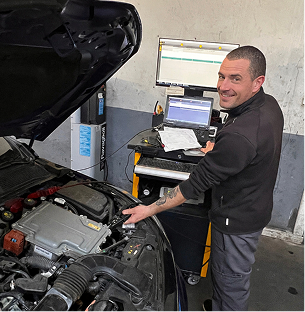 Mécanicien souriant inspectant un moteur de voiture ouvert, avec des écrans d'ordinateur de diagnostic à Saint-Orens près de Toulouse en Haute-Garonne 31
