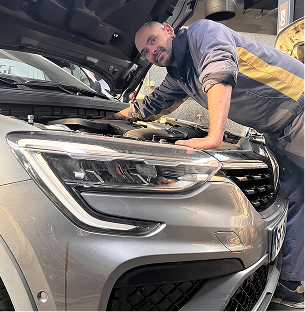 Mécanicien masculin chauve penché sur le moteur ouvert d'une voiture grise, vous regarde à Saint-Orens près de Toulouse en Haute-Garonne 31