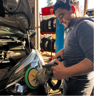 Homme souriant polissant un phare de voiture dans un garage, pneus en arrière-plan à Saint-Orens près de Toulouse en Haute-Garonne 31