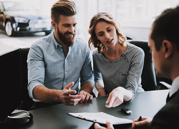 Couple heureux discutant des conditions avec un vendeur de voitures.